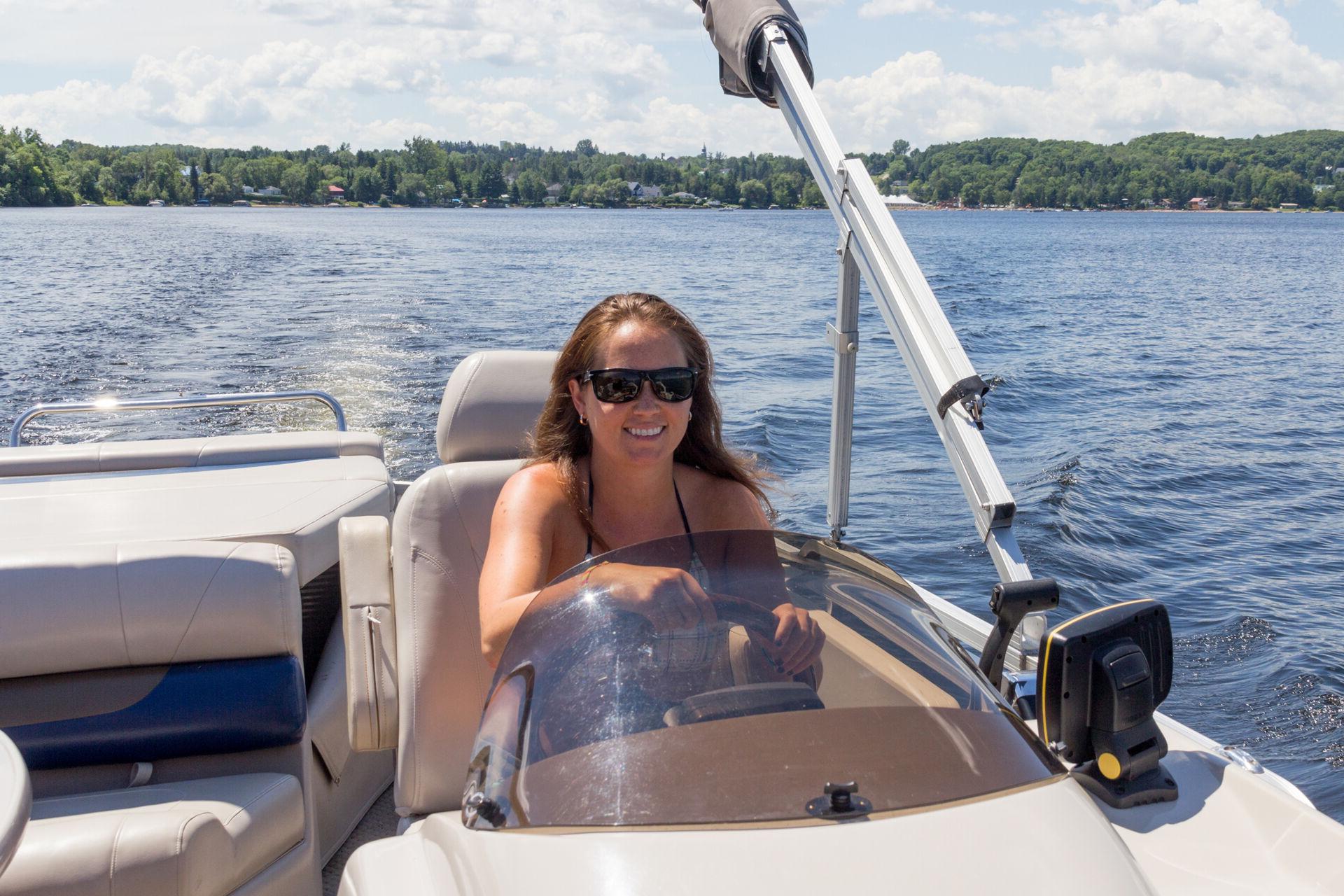 A woman is smiling while she drives the new boat she got with credit union financing.